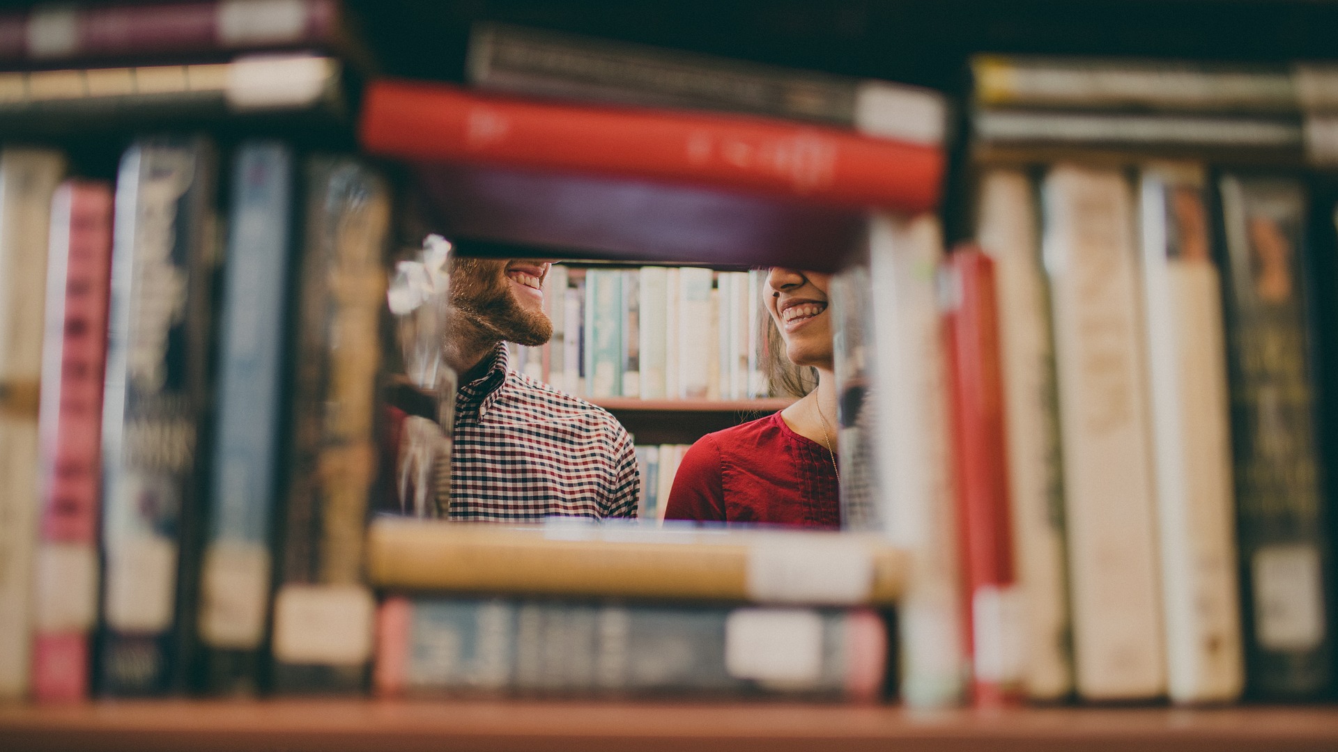 Books on shelf in rectangular formation with an opening in the middle showing the bottoms of two smiling faces.