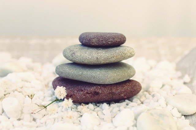 Pile of four flat stones, two burgundy on the top and bottom of the pile, two gray ones in the middle, on a pile of white crunchy pebbles, with a tiny white flowers in the foreground in the bottom left corner